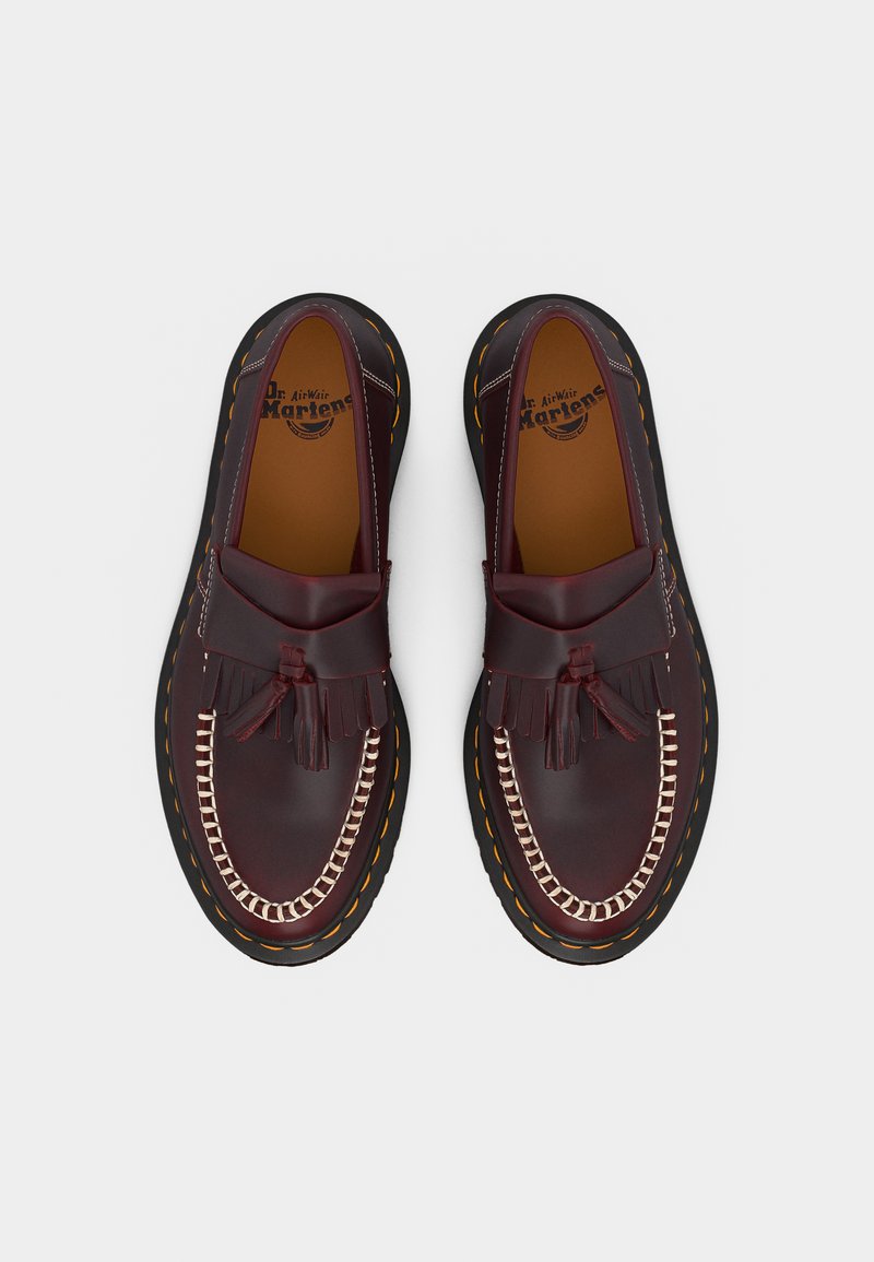 Coppia di mocassini con nappe in pelle bordeaux lucidati, con cuciture bianche e suole nere con cuciture gialle, visti dall'alto.