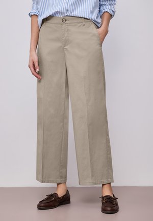 Kvinde iført beige bukser med vide ben, blå- og hvidstribet skjorte stoppet ind, med mørkebrune snørebådssko.