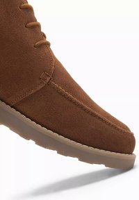 Brun mocka ankle boot med rund tå, med ton-i-ton snörning och sömmar, samt en gummisula med ett strukturerat mönster.