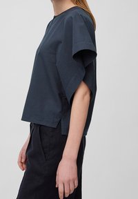 Top corto navy scuro con maniche corte e vestibilità rilassata, caratterizzato da un collo rotondo e fessure laterali. Realizzato in tessuto testurizzato con una forma leggermente strutturata.