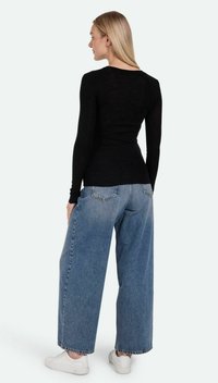 Schwarzes Langarmoberteil mit einem figurbetonten Design, kombiniert mit hellblauen weiter geschnittenen Jeans und weißen Sneakers. Glatte Textur und schlichte Stilrichtung.