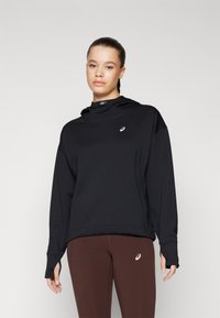 Black hoodie with a high neck, soft texture, and a small logo on the chest. Paired with dark brown leggings featuring a subtle logo.