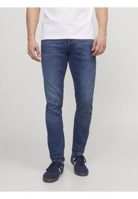 Modré džíny z denimu se slim střihy, s kontrastním prošíváním, pětipocket designem a hladkou texturou. Nosí se s námořnickými teniskami.