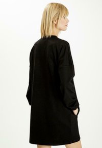 Czarna sukienka dresowa z długimi rękawami, okrągłym dekoltem i bocznymi kieszeniami. Wykonana z miękkiego materiału, charakteryzująca się luźnym krojem i gładką teksturą.
