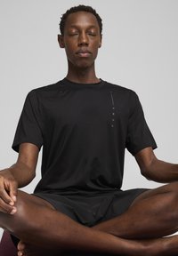 Sort atletisk T-shirt med korte ærmer, lavet af et glat, let stof; har et lodret hvidt "PUMA" logo på venstre side.