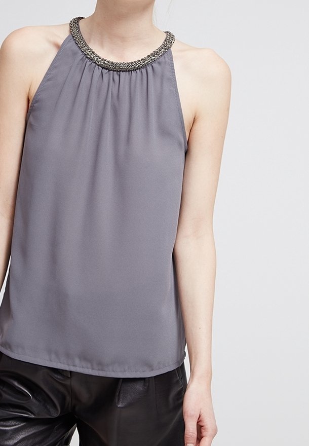 Haut gris sans manches à col licou tressé décoratif porté avec un pantalon en cuir noir.