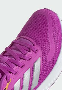 Baskets de sport violettes avec une tige en maille, des accents texturés et des bandes réflectrices argentées. Les lacets sont également violets, avec un design robuste.