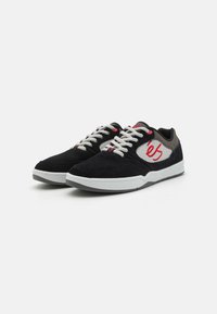 Baskets en daim noir avec une semelle en caoutchouc blanche, des accents gris et un logo rouge sur le côté. Dotées de lacets blancs et de détails en relief.