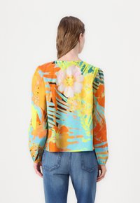 Blouse à manches longues avec un imprimé floral et de palmiers vibrant dans des teintes d'orange, de bleu et de jaune, fabriquée en tissu léger et offrant une coupe décontractée.