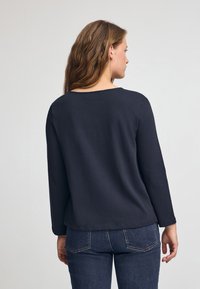 Mörk marinblå långärmad topp med rund halsringning och avslappnad passform, tillverkad av ett slätt tyg, parat med jeans i denim med bakfickor.