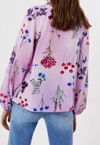 Långärmad blus i ljuslila, med blommönster i blått, rött och grönt. Mjukt tyg med skräddade manschetter och en avslappnad passform.