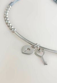 Silberarmband mit herzförmigen Schloss- und Schlüsselanhängern, gebogenes Design mit glatten und perlbesetzten Abschnitten auf hellem Hintergrund.