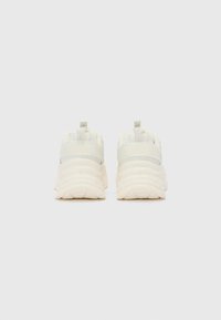 Chunky white sneakers with textured fabric, elastic straps, and a raised sole. Featuring reinforced back tabs for easy wear.