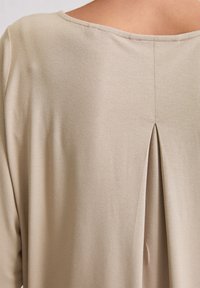 Beige top med blød tekstur og afslappet pasform. Har en bred udskæring og en lille plissé bagpå for ekstra detaljer.