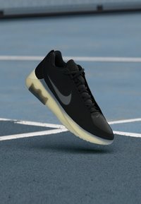 Čierne športové topánky s textúrovaným zvrškom, s šedým logom Nike a priesvitnou svetlou podrážkou. Navrhnuté pre atletický výkon.