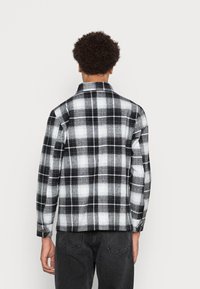 Svart och vit rutig flanellskjorta med knappad krage, långa ärmar och en strukturerad tyg. Har en avslappnad passform och bakstycke.
