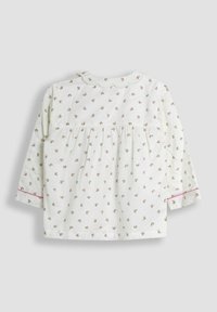 Blusa bianca a maniche lunghe con piccolo motivo floreale rosa, colletto ondulato e design della parte posteriore arricciato. Presenta accenti rosa sui bordi delle maniche.