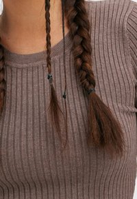 Maglione marrone a coste con scollatura rotonda, caratterizzato da un motivo testurizzato. Due ciocche di capelli intrecciati sono visibili, con elastici neri.