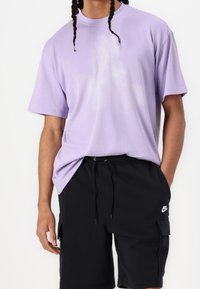 Jasnoliliowa bawełniana koszulka z krótkim rękawem i okrągłym dekoltem, połączona z czarnymi szortami z bocznymi kieszeniami i małym białym logo.