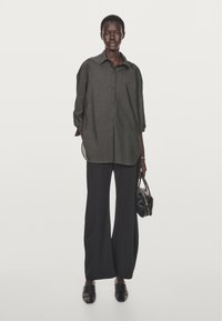 Übergroßes, dunkelgraues Hemd mit hochgekrempelten Ärmeln, kombiniert mit weiten schwarzen Hosen und einer kleinen, strukturierten schwarzen Handtasche.