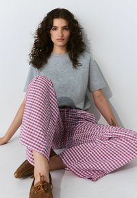 Grijze korte mouwen t-shirt gecombineerd met brede, rood en blauw geruite broek met een trekkoord en bruine instappers.