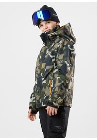 Kamouflage vattentät jacka i grönt och brunt med orange dragkedjedetaljer, hög krage och åtsittande ärmar, bärs med skidglasögon och en svart mössa.