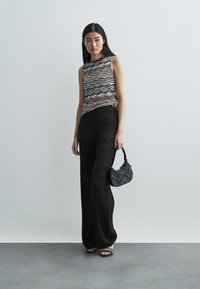 Top de malha com padrão de zig-zag multicolorido, combinado com calças pretas de perna larga. Leva uma pequena bolsa multicolorida texturizada.