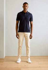 Marineblå polo skjorte med en subtil logo, paret med lyse beige bukser og hvite sneakers. Glatt stoff, tettsittende design og klassisk krage.