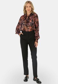 Czarne spodnie z wysokim stanem w połączeniu z przezroczystą bluzką w wzory paisley w odcieniach fioletu, różu i pomarańczy.