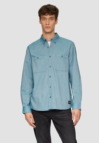 Lichtblauw overhemd met knopen, gemaakt van denim, met twee borstzakken, lange mouwen en een ronde zoom. Gestyled met een donkere denim achtergrond.