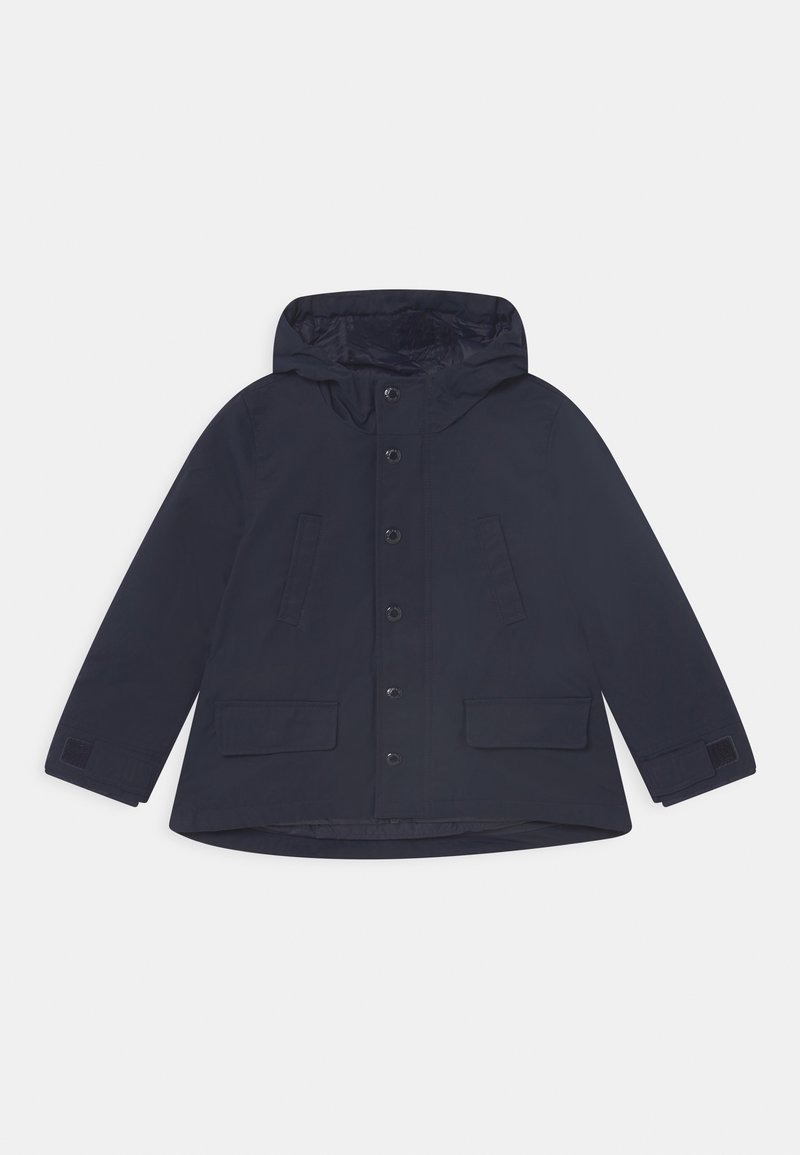 Marinblå huvjacka med knappstängning, två framfickor och kardborreband vid ärmsluten. Tillverkad av vattentåligt material.