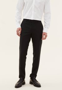 Pantaloni neri su misura realizzati in tessuto morbido, con una vestibilità slim, passanti per cintura e chiusura con un solo bottone, abbinati a scarpe eleganti nere.