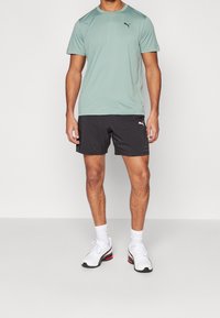 T-shirt atlético de hombre en verde claro, pantalones cortos negros y zapatillas blancas. Incluye material que absorbe la humedad y acentos con el logo de la marca.