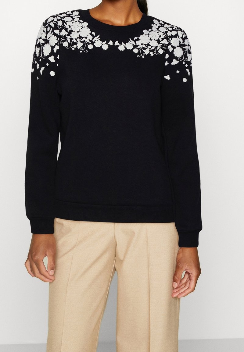 Marineblauer Pullover mit langen Ärmeln, verziert mit weißer Blumenstickerei über den Schultern. Gerippte Bündchen und Saum; weicher, strukturierter Stoff.