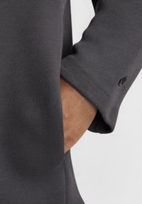 Ciemnoszara bluza z gładką fakturą, z kieszenią po boku oraz subtelnym, haftowanym logo na rękawie.