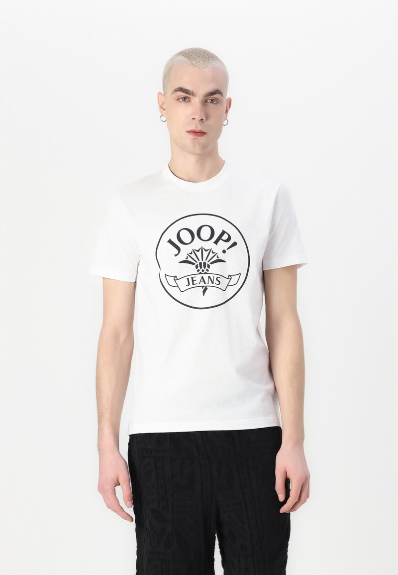 Bílá bavlněná tričko s kulatým grafickým logem "JOOP! JEANS" v černé barvě, uprostřed stylizovaného květinového motivu. Krátké rukávy, kulatý výstřih.