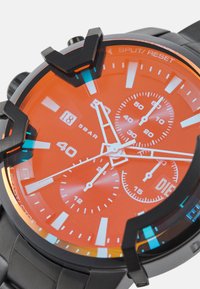 Chronograph-Uhr mit einem hellorangen Zifferblatt, schwarzem Gehäuse, mehrfarbigen Akzenten, weißen Markierungen und einem strukturierten Armband; wasserdicht bis 5 bar.