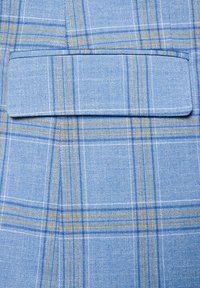 Jasnoniebieska tkanina w kratę z cienkimi żółtymi i ciemnoniebieskimi liniami. Widoczna jest naszywana kieszeń zintegrowana z wzorem. Teksturowany splot.