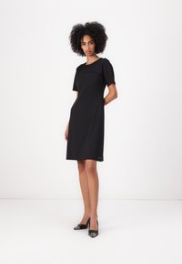Rochie scurtă neagră cu un design structurat, până la genunchi, cu un guler rotund și detalii la cusăturile laterale. Purtați-o cu tocuri negre.