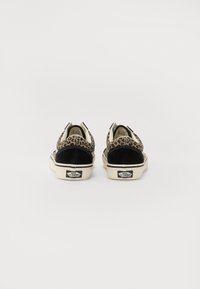 Une paire de baskets Vans avec un imprimé léopard et un talon noir, vue de dos sur un fond blanc uni.