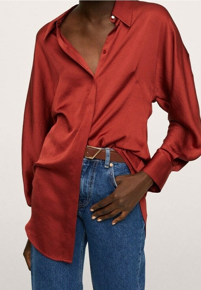 Chemise rouge en satin à boutons avec manches longues, poche avant et ourlet légèrement arrondi, associée à un jean en denim bleu et une ceinture marron.