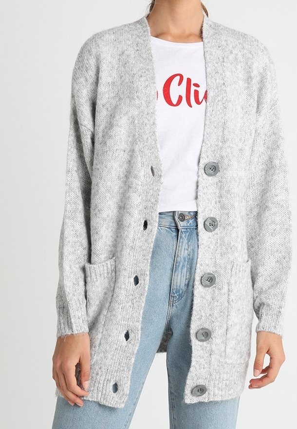Femme portant un cardigan en laine gris clair avec de gros boutons par-dessus un t-shirt blanc à motif graphique et un jean taille haute bleu clair.