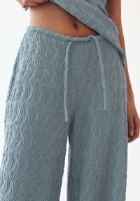 A pair of light blue, textured pants with a wavy pattern, featuring an elastic waistband and drawstring for adjustment.
