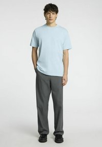 Šviesiai mėlyna trumpomis rankovėmis marškinėlė, laisvas pritaikymas, dėvima su tamsiai pilkiais klostuotais kelnėmis ir juodais batais. Paprastas dizainas be matomų raštų.