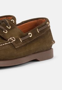 Καφέ σουέντ παπούτσι τύπου boat με δερμάτινα κορδόνια περασμένα μέσα από χρυσά μεταλλικά δακτυλίδια και ταμπά ελαστική σόλα.