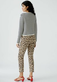 Gestreifter Pullover in Schwarz und Weiß, kombiniert mit hellbraunen Leopard-Print-Hosen und roten Absatzsandalen. Strukturierter Stoff, taillierte Silhouette.