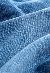 Țesătură de denim de culoare albastră deschisă, cu o țesătură texturată, cu fire vizibile și variații subtile de culoare, evidențiind profunzimea și finețea.