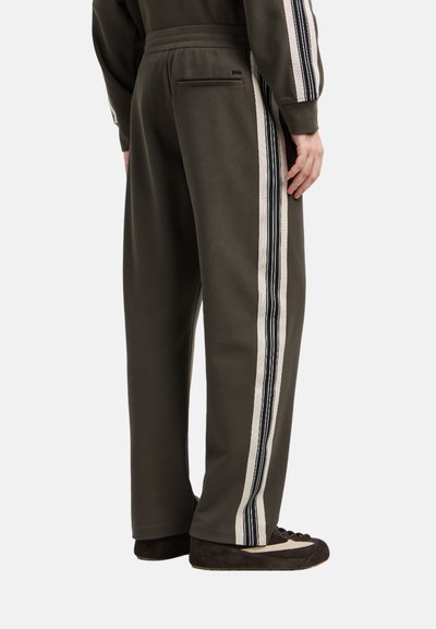 Pantaloni della tuta verde oliva con vestibilità rilassata, caratterizzati da strisce laterali in crema e blu scuro, texture morbida e una piccola tasca posteriore.