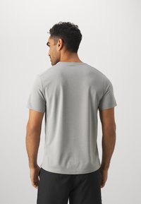 T-shirt gris à manches courtes en tissu doux, avec un col rond et une texture lisse. L'arrière ne présente aucune décoration ni motif.