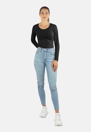 Schwarzes Langarm-T-Shirt mit Rundhalsausschnitt, kombiniert mit hellblauen hochgeschnittenen Jeans und weißen Sportschuhen.